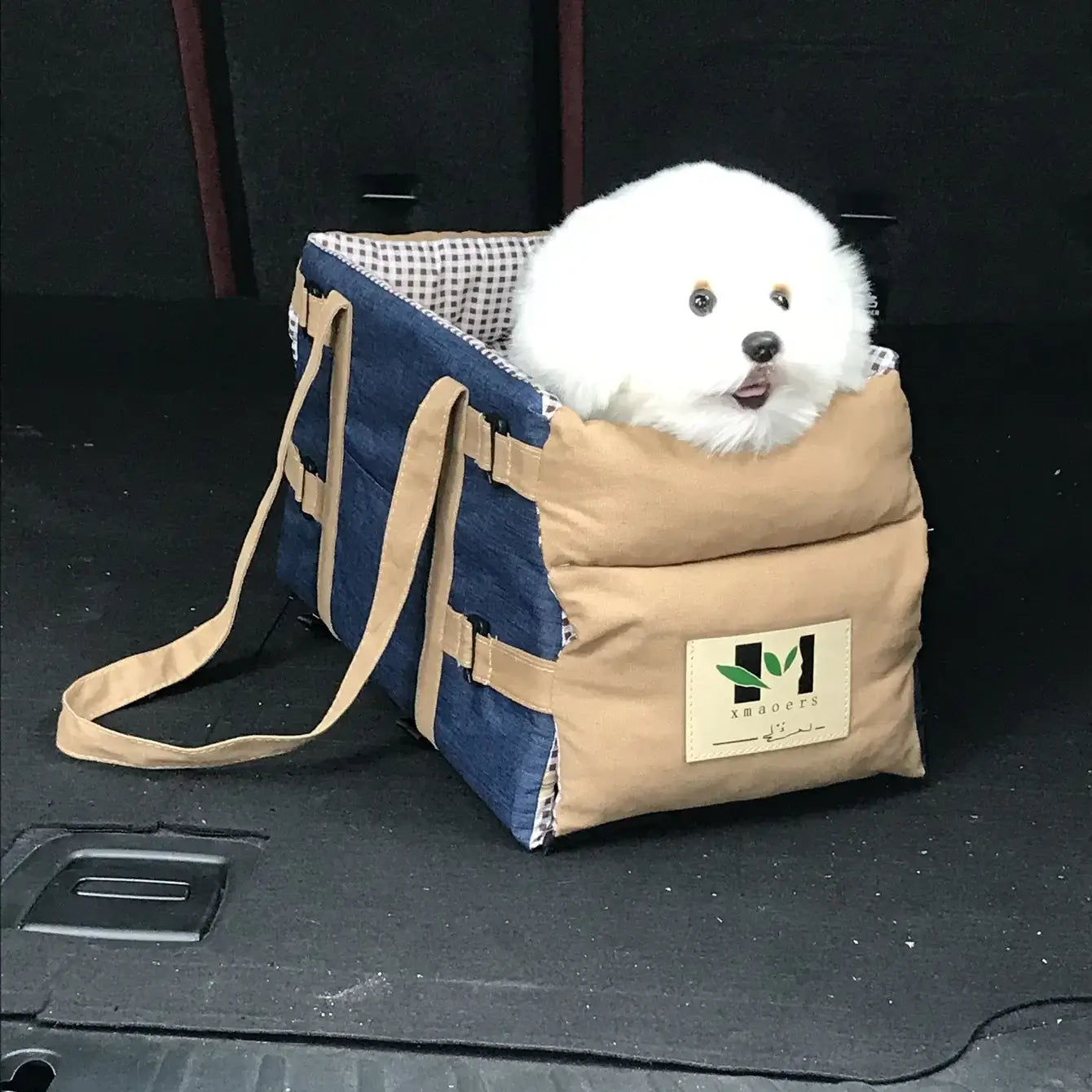 Plush white dog sitting comfortably in a stylish tan and blue car seat for safe travel.